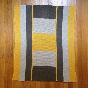 May include: A knitted throw blanket with a geometric pattern in shades of gray, yellow, and light gray.