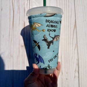 May include: A blue and white reusable cup sleeve with a dragon pattern and the text "Dragons always know fly or die".