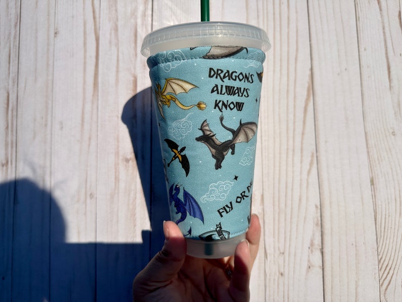 May include: A blue and white reusable cup sleeve with a dragon pattern and the text "Dragons always know fly or die".