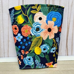 May include: A navy blue fabric cup cosy with a floral pattern featuring pink, orange, yellow, and blue flowers. The fabric has a white background with a dark blue outline.