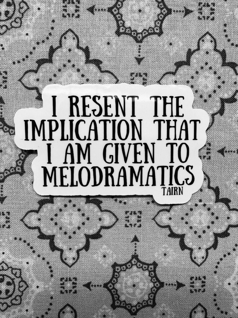 Puede incluir: Una pegatina blanca con texto negro: "I RESENT THE IMPLICATION THAT I AM GIVEN TO MELODRAMATICS", con "TAIRN" debajo. La pegatina est&aacute; sobre un fondo con estampado gris y blanco.
