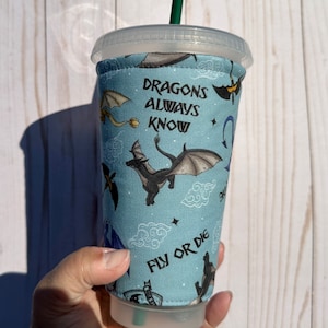 May include: A blue and black reusable cup sleeve with a dragon pattern and the text "Dragons Always Know Fly Or Die".