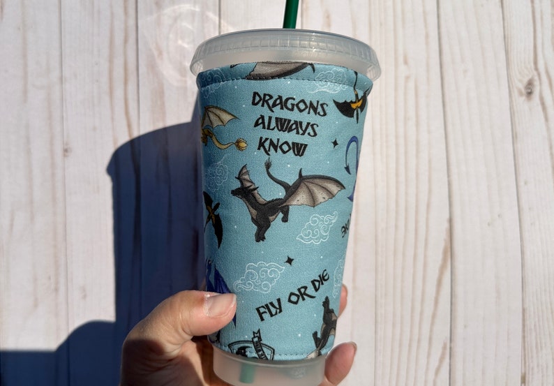 May include: A blue and black reusable cup sleeve with a dragon pattern and the text "Dragons Always Know Fly Or Die".