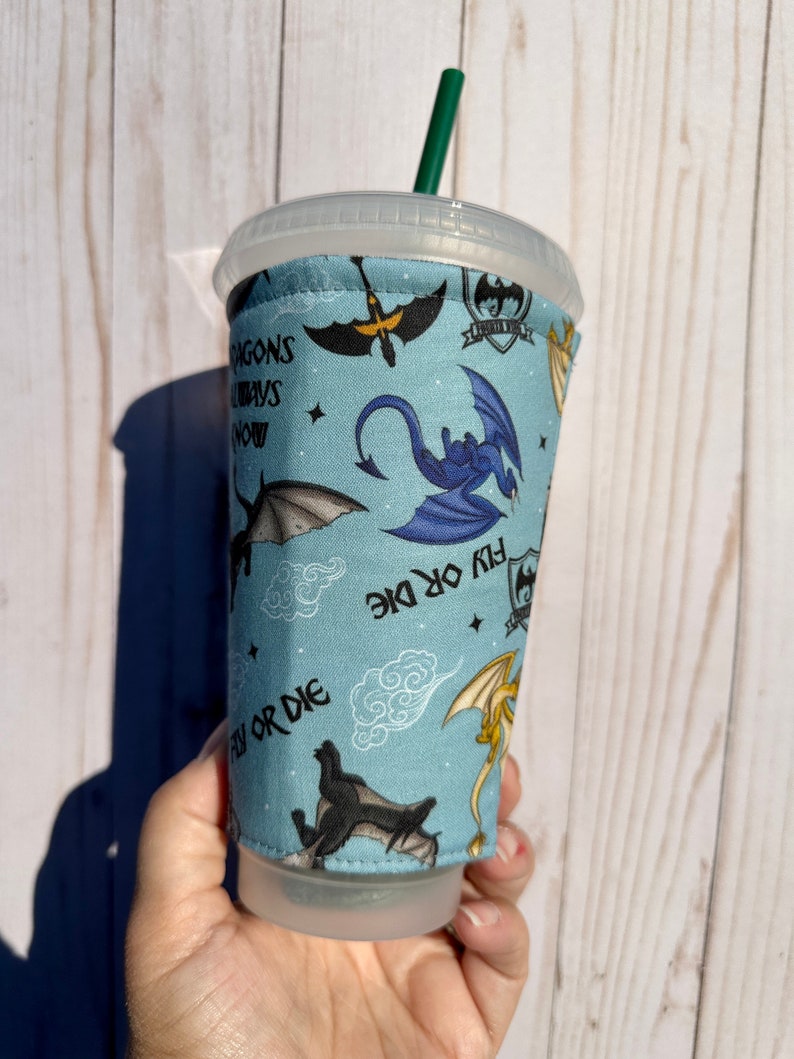 May include: A blue reusable cup sleeve with a dragon design. The sleeve features multiple dragons in various poses, including flying, perched, and in mid-air. The text "Fly or Die" is repeated on the sleeve.