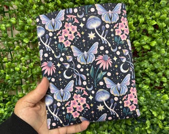 May include: A dark fabric item with a repeating pattern of butterflies, mushrooms, flowers, moons, and stars. The butterflies are light blue and purple, and the flowers are pink. The background is black.