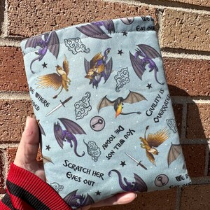 May include: A blue book sleeve with a repeating pattern of dragons, birds, and clouds. The text "We Eat Our" and "Civility is Overrated" is printed on the sleeve.