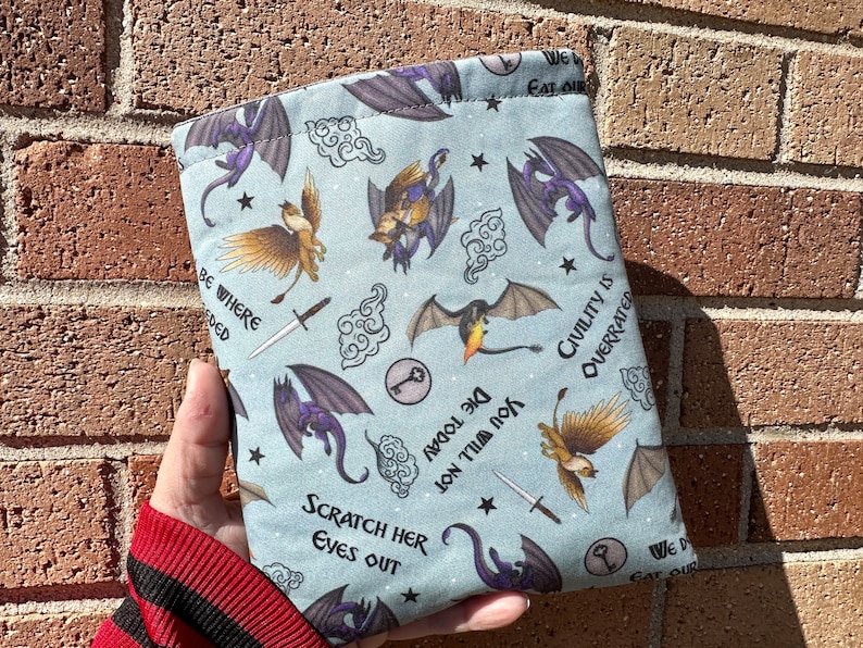 May include: A blue book sleeve with a repeating pattern of dragons, birds, and clouds. The text "We Eat Our" and "Civility is Overrated" is printed on the sleeve.