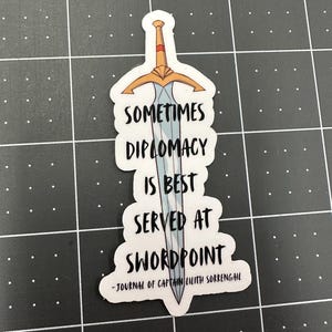 Puede incluir: Una pegatina con un dise&ntilde;o de espada y la cita "Sometimes diplomacy is best served at swordpoint - Journal of Captain Lilith Sorrengail".