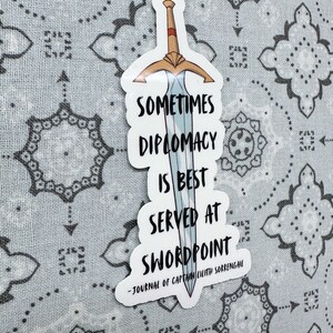 Puede incluir: Una pegatina blanca con una espada azul y el texto "Sometimes diplomacy is best served at swordpoint - Journal of Captain Lilith Sorrengail"
