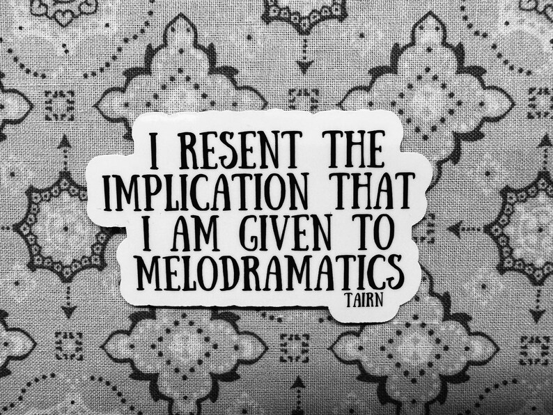 Puede incluir: Una pegatina blanca con texto negro: "I RESENT THE IMPLICATION THAT I AM GIVEN TO MELODRAMATICS" y el nombre "TAIRN" debajo. Sobre un fondo gris con estampado.