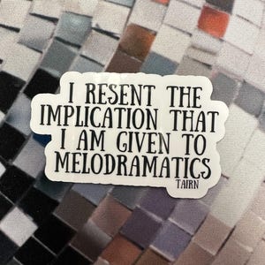 May include: White sticker with the text "I RESENT THE IMPLICATION THAT I AM GIVEN TO MELODRAMATICS" in a bold, black font. The sticker has a white border and the word "TAIRN" at the bottom. The background is a mosaic pattern of various colors.