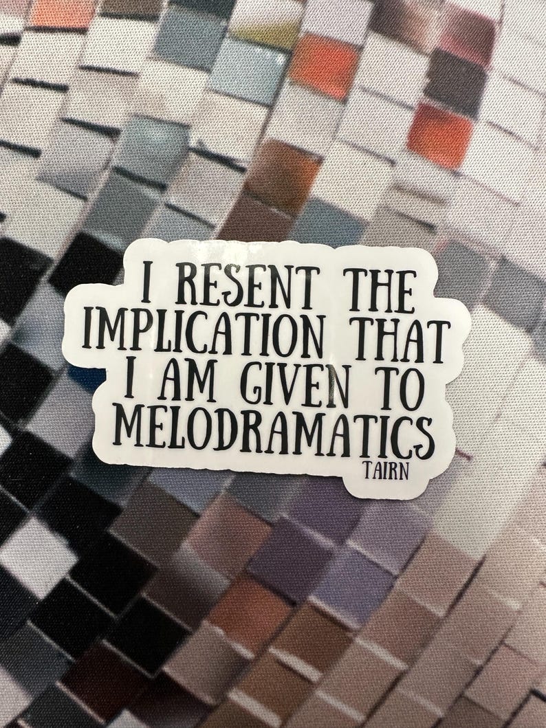 Puede incluir: Pegatina blanca con el texto "I RESENT THE IMPLICATION THAT I AM GIVEN TO MELODRAMATICS" en negrita y en negro. La pegatina tiene un borde blanco y la palabra "TAIRN" en la parte inferior. El fondo es un patr&oacute;n de mosaico.