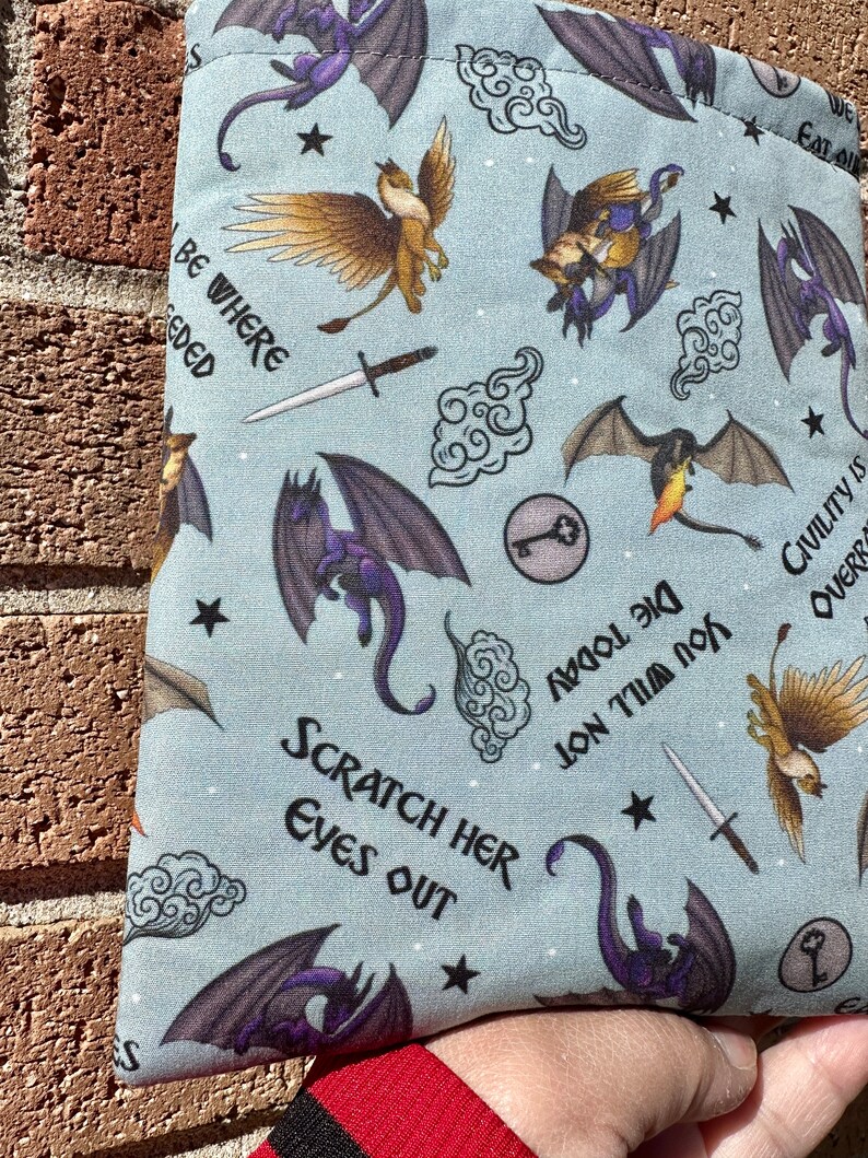 May include: A blue fabric pouch with a repeating pattern of dragons, griffins, swords, keys, clouds, and stars. The pouch has the text "Be Where Needed", "Scratch Her Eyes Out", "Die Today You Will Not", and "Civility is Overrated".