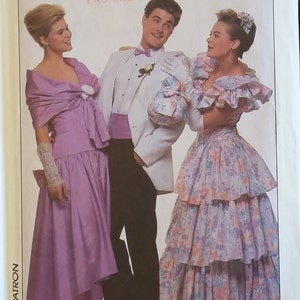 May include: A vintage sewing pattern featuring three people in formal attire. The woman on the left is wearing a purple dress with a ruffled neckline and a matching shawl. The woman on the right is wearing a tiered floral dress with a ruffled neckline and a white bow. The man in the middle is wearing a white tuxedo with a black bow tie and a white flower on his lapel. The pattern is titled "The Accessory Club".