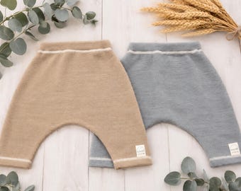 May include: Two pairs of knit pants, one in tan and one in slate blue, featuring a high-waisted design with a thin white horizontal stripe at the waistband and cuffs. Each pair includes a small white rectangular label with a rainbow icon and text.