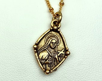 May include: Gold chain necklace with a gold pendant featuring a religious image of a woman holding a cross. The pendant is in the shape of a diamond.