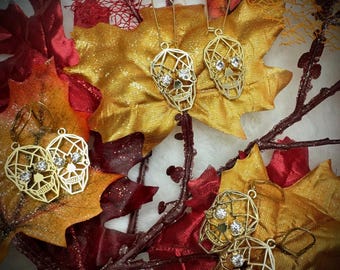 May include: Gold geometric skull earrings with clear rhinestone accents. The earrings are displayed on a background of fall leaves.