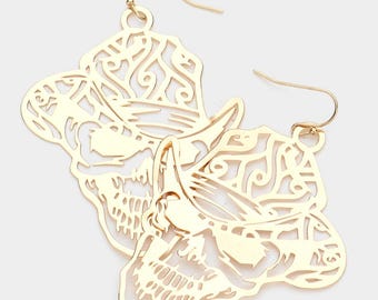 May include: Gold-colored earrings featuring a cowboy hat design. The earrings have a filigree pattern and a hook closure. The hat design is detailed with cut-out shapes and a curved brim, creating a delicate and stylish accessory.