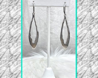 May include: A pair of silver dangle earrings with an open oval design. The earrings are displayed on a white stand.