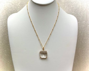 May include: A gold chain necklace with a clear square pendant. The pendant has a faceted design.