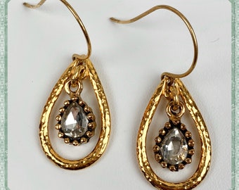 May include: Gold teardrop earrings with a clear crystal stone in the center of each teardrop. The teardrops have a textured surface and a delicate wire loop.