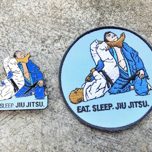 Puede incluir: Un conjunto de pin y parche con temática de Jiu Jitsu. El pin es rectangular y el parche es circular. Ambos artículos representan una escena de artes marciales en azul, blanco y beige, con el texto "EAT. SLEEP. JIU JITSU."
