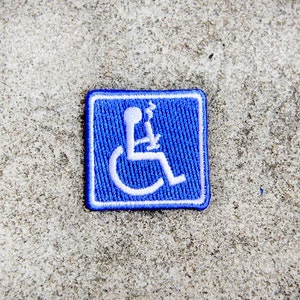 May include: A square, blue patch featuring a white embroidered image of a person in a wheelchair holding a smoking device. The patch has a white border and is set against a textured, grey background.