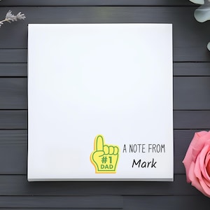 May include: A white card with a green and yellow cartoon hand with a finger pointing up. The hand has the text "#1 Dad" on it. The card also has the text "A note from Mark" on it.