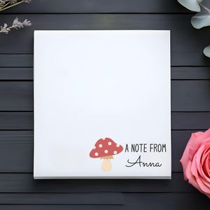 May include: A white notepad with a red and white mushroom illustration and the text "A note from Anna". The notepad is on a dark wood surface with lavender and eucalyptus sprigs.