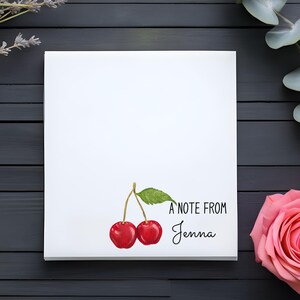 May include: A white card with a watercolor illustration of two red cherries with green stems and leaves. The text "A note from Jenna" is written in black below the cherries.