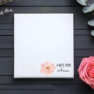 May include: A white notepad with a pink flower illustration and the text "A note from Anna". The notepad is on a dark wood surface with lavender and eucalyptus branches.