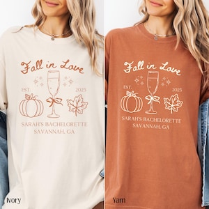 May include: Ivory and yam-colored t-shirts with the text "Fall in Love" and "Sarah's Bachelorette Savannah, GA." The design includes a champagne glass, pumpkin, and leaf.
