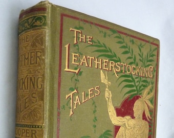 May include: A vintage book titled "The Leatherstocking Tales" by J. Fenimore Cooper. The cover features a green background with gold lettering and illustrations of a Native American man holding a spear and a leafy design.