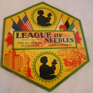 May include: Vintage hexagonal sewing needle packaging with a yellow background and green trim. The packaging features the text "LEAGUE OF NEEDLES" and illustrations of flags, silhouettes, and landmarks. The text "MADE IN JAPAN" is also visible.