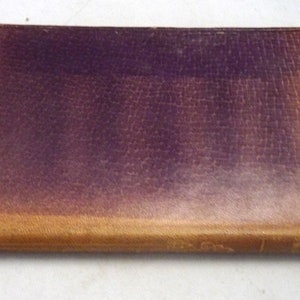 May include: A vintage leather-bound book with a dark purple cover and a light brown spine.