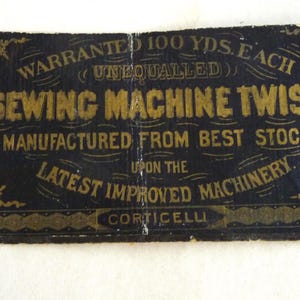 May include: A vintage sewing machine twist label with gold lettering on a dark blue background. The label reads "Warranted 100 yds. Each" and "Sewing Machine Twist." The text also includes "Manufactured from Best Stock" and "Latest Improved Machinery."