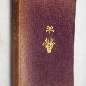 May include: A burgundy leather-bound book with gold lettering and a gold floral design on the front cover. The title of the book is "Days of the Year".