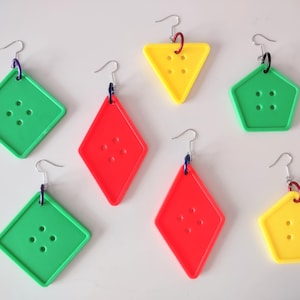Puede incluir: Seis pares de pendientes coloridos con formas geométricas. Cada pendiente presenta un color y una forma diferentes, incluyendo rojo, verde y amarillo. Los pendientes están hechos de plástico y tienen un diseño de botón con agujeros.