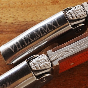 K&ouml;nnte beinhalten: Ein silberner Korkenzieher mit einem Holzgriff. Der Korkenzieher hat ein dekoratives Design und das Datum "VII.IX.MMXI" ist in das Metall graviert.
