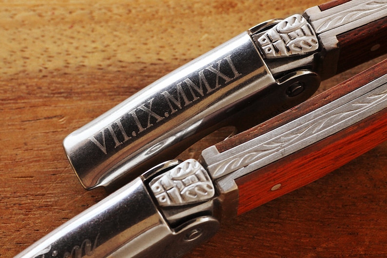 K&ouml;nnte beinhalten: Ein silberner Korkenzieher mit einem Holzgriff. Der Korkenzieher hat ein dekoratives Design und das Datum "VII.IX.MMXI" ist in das Metall graviert.