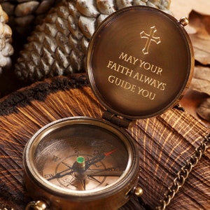 May include: A brass compass with a chain attached. The compass lid is open and features an inscription that reads "May your faith always guide you" with a cross above the text.