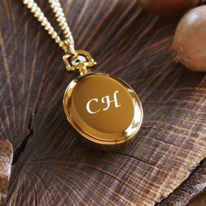 Peut inclure: Une montre de poche dorée avec une chaîne sur une surface en bois. Le cadran de la montre est gravé des initiales "CH".