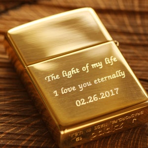 May include: A gold-colored metal lighter with engraved text: "The light of my life, I love you eternally, 02.26.2017." The lighter is rectangular and has a hinged lid. The brand name and location are also engraved.