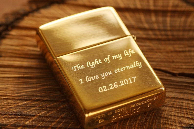 May include: A gold-colored metal lighter with engraved text: "The light of my life, I love you eternally, 02.26.2017." The lighter is rectangular and has a hinged lid. The brand name and location are also engraved.