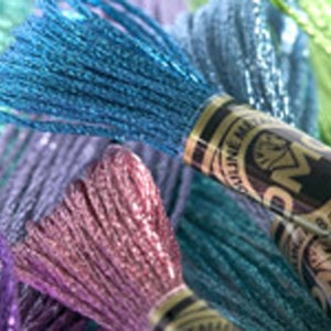 May include: Close-up of a variety of colorful embroidery floss spools with metallic threads. The spools are labeled "DMC Coloris" and feature a diamond logo.