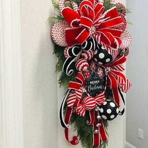 May include: A red and white Christmas swag with a large red velvet bow, candy cane ornaments, and a sign that says "Merry Christmas".