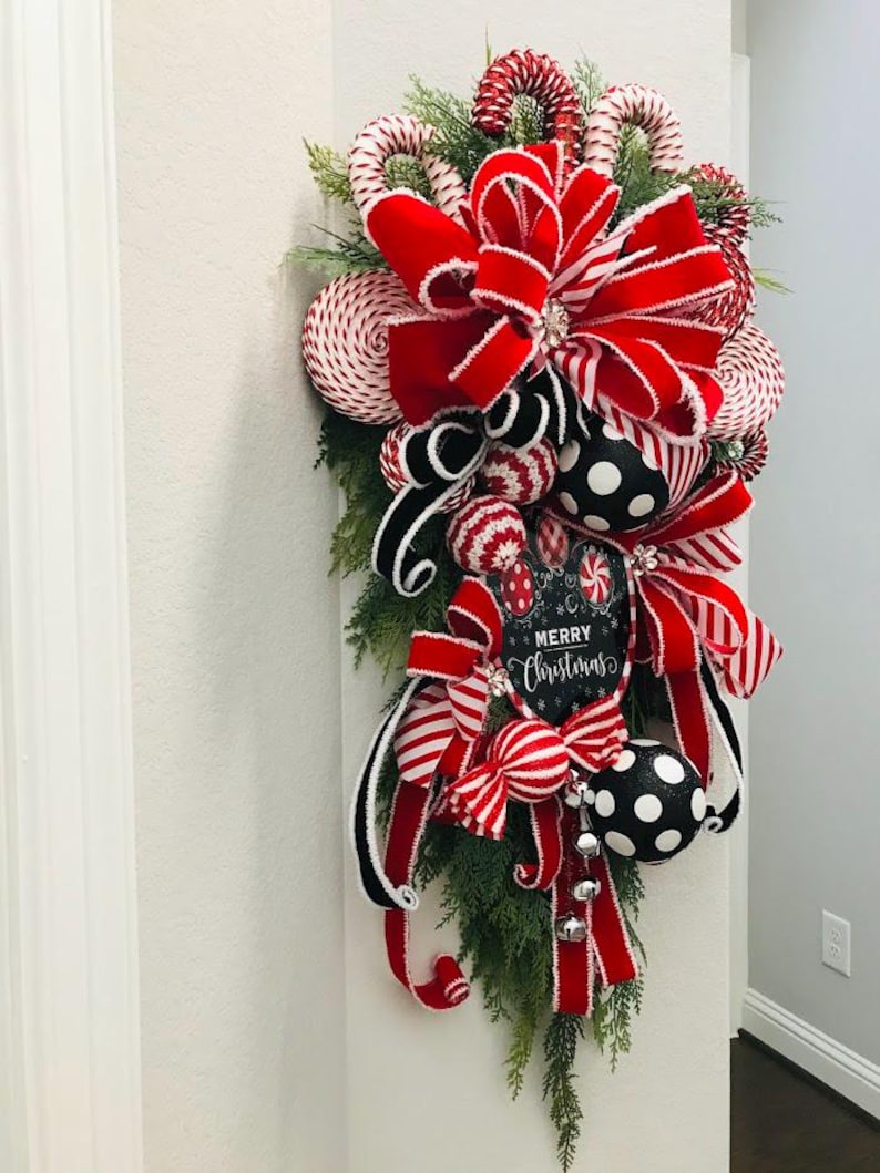 May include: A red and white Christmas swag with a large red velvet bow, candy cane ornaments, and a sign that says "Merry Christmas".