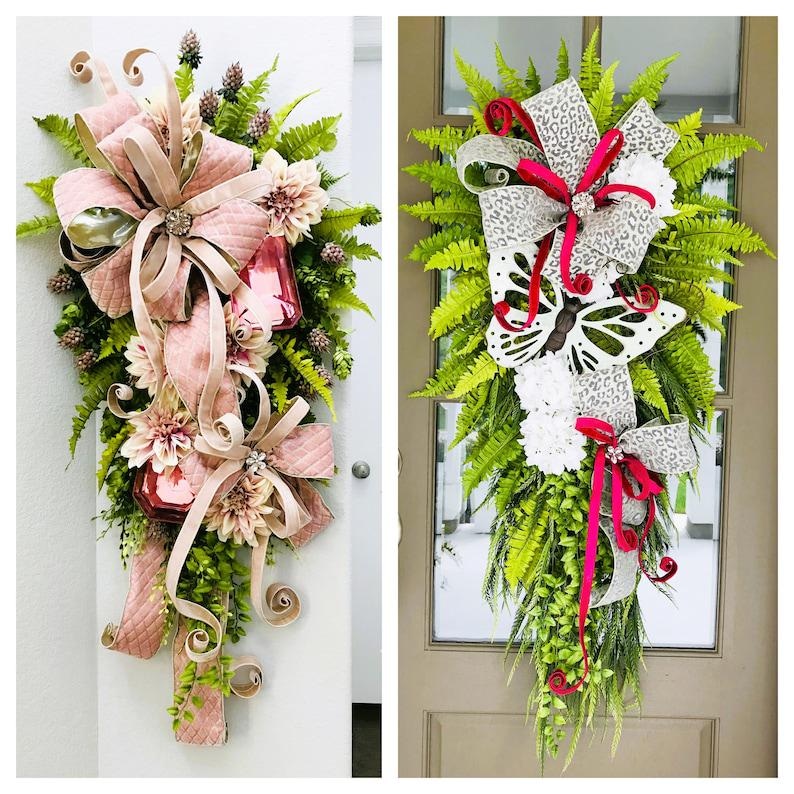 May include: Two door wreaths with pink and white bows, greenery, and flowers. One wreath has a pink bow and the other has a white bow with a butterfly.