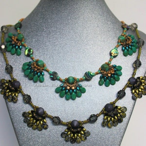 Puede incluir: Dos collares de cuentas expuestos en un maniquí. El collar superior presenta cuentas turquesas y marrones con acentos iridiscentes. El collar inferior tiene cuentas grises y doradas. El texto "ABIGAIL ELIZABETH DESIGNS" es visible.