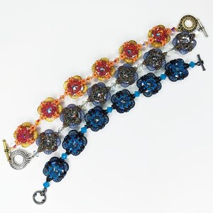 May include: Three beaded bracelets with floral designs in shades of red, purple, and blue. Each bracelet features a toggle clasp and is adorned with sparkling beads. The bracelets are arranged diagonally against a white background.